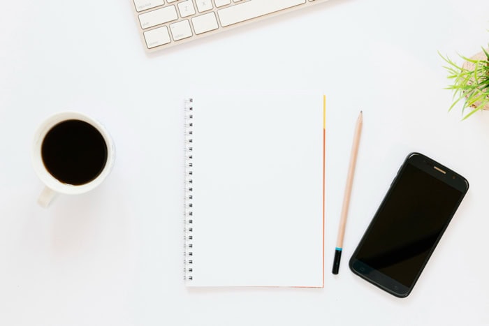 Carnet, crayon, smartphone et café sur un bureau, symbolisant l'organisation et la recharge de l'énergie